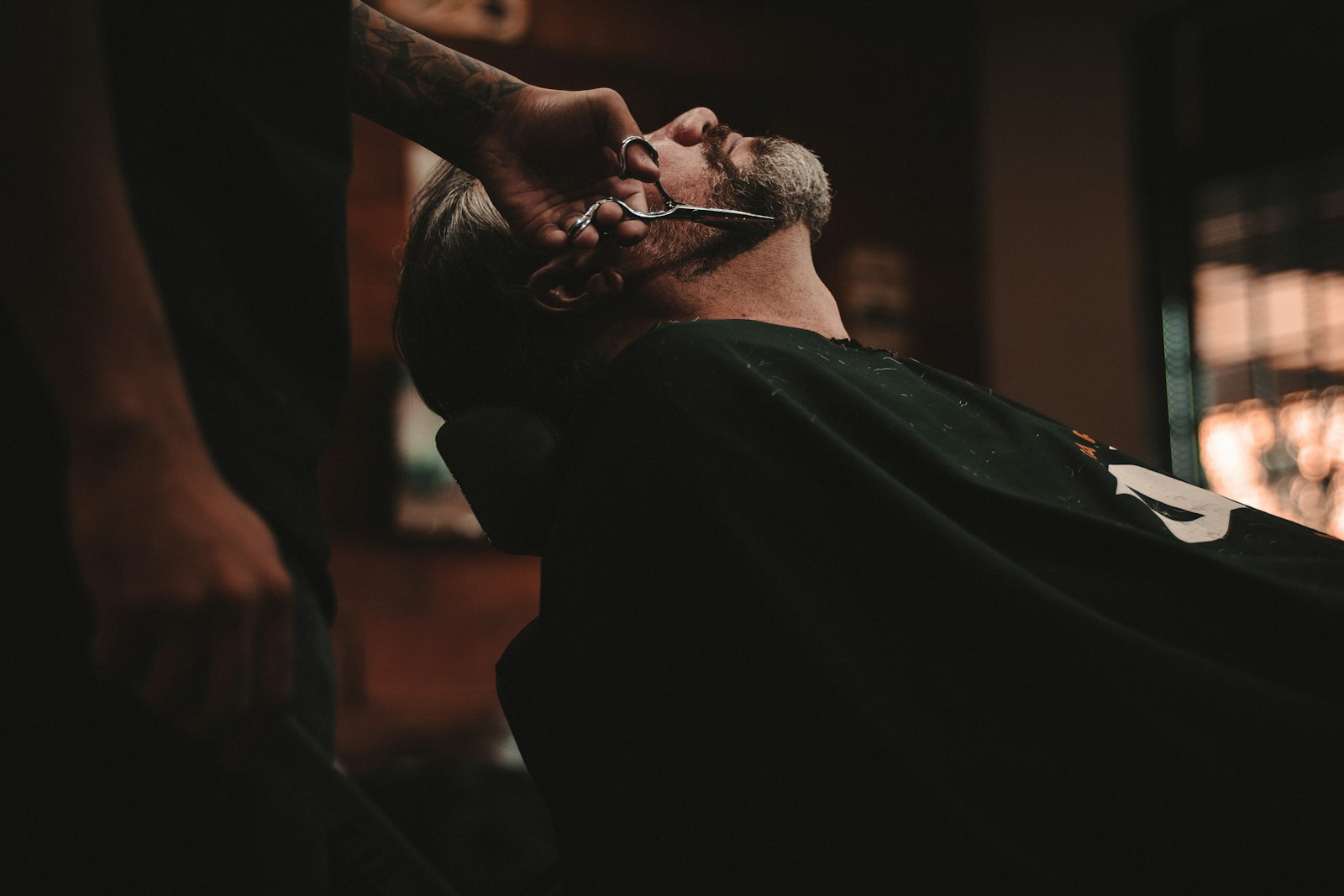 A barber carefully shaping a client's fade inside a warm, classic barber shop.